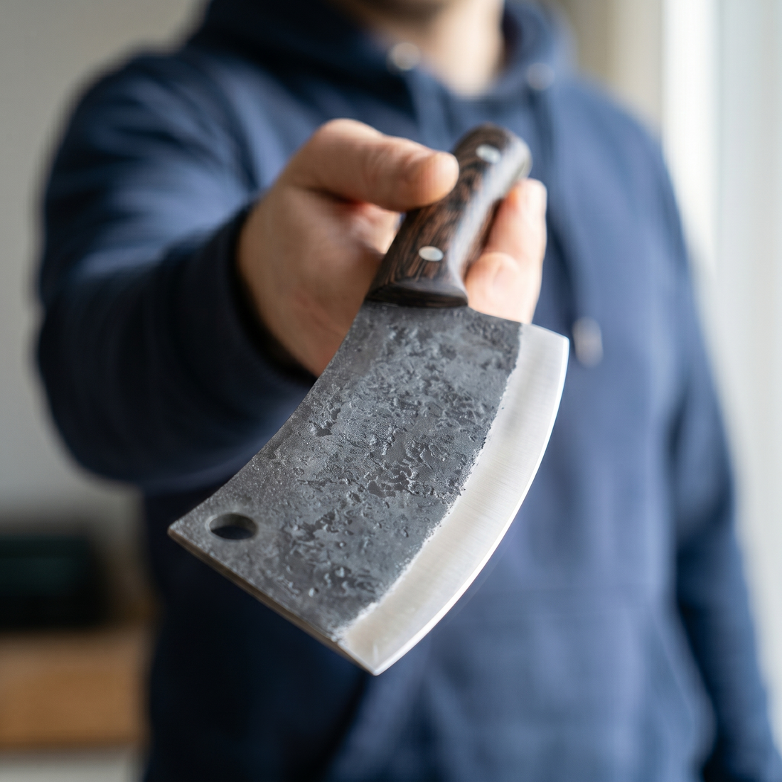 Hand forged Serbian style cleaver with a finger hole and dark wood handle, held out toward the camera
